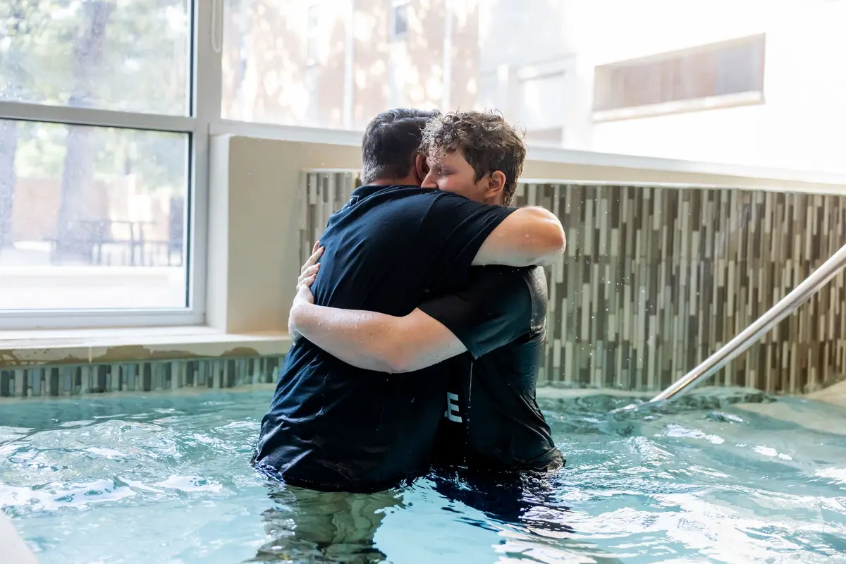 Two men hugging in an indoor baptism pool right after a baptism