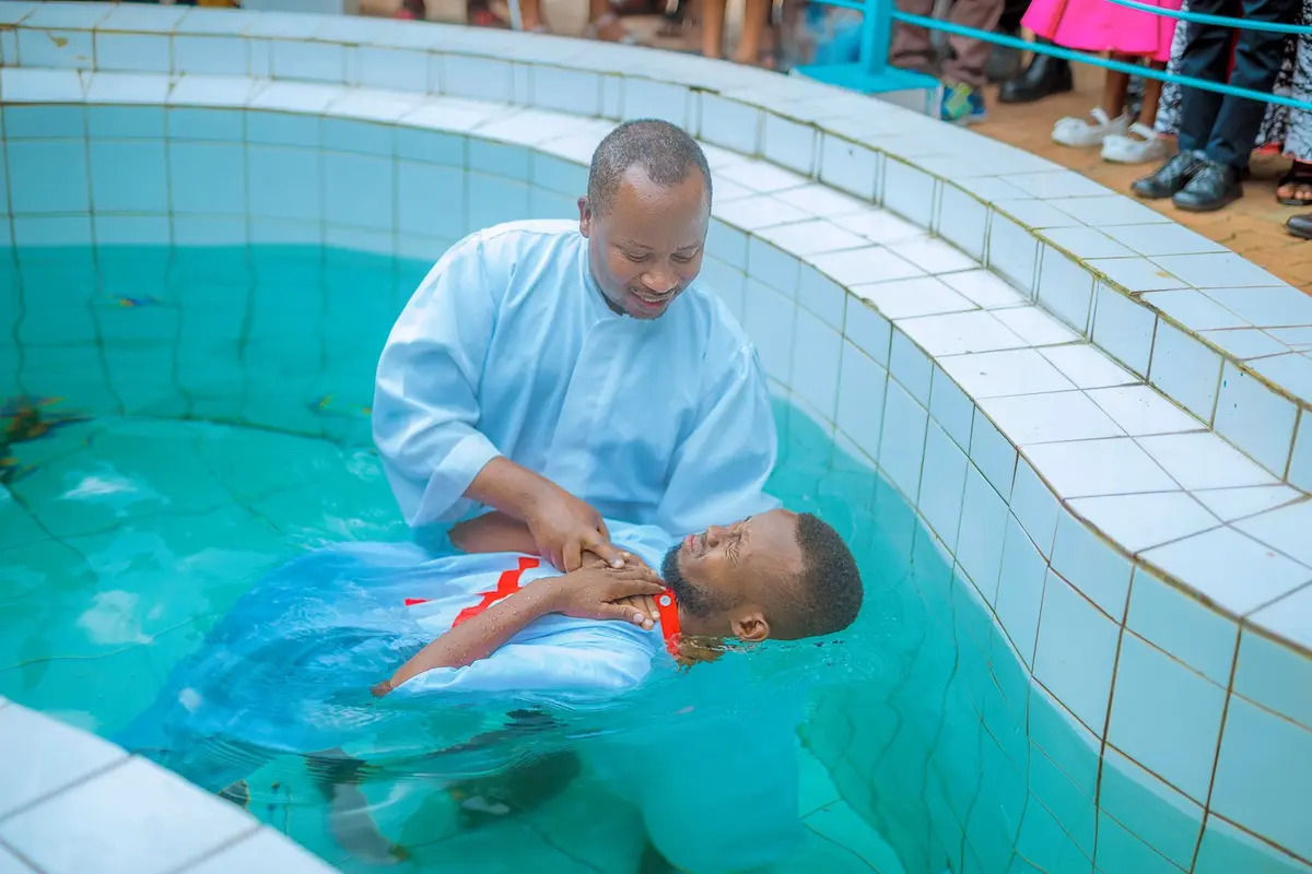 A pastor baptizing a man in an outdoor pool while people watch from the edge