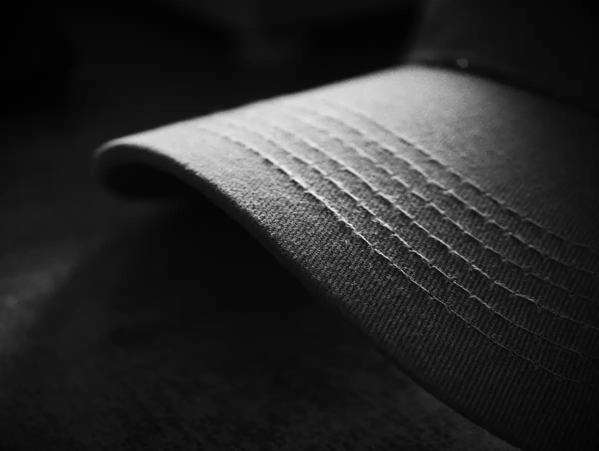 Black and white close-up of the stitched bill of a baseball cap