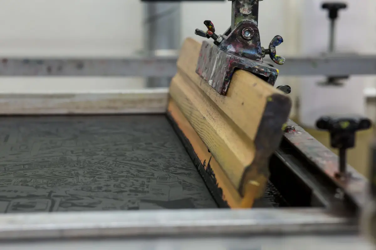A wooden squeegee resting on a screen printing press