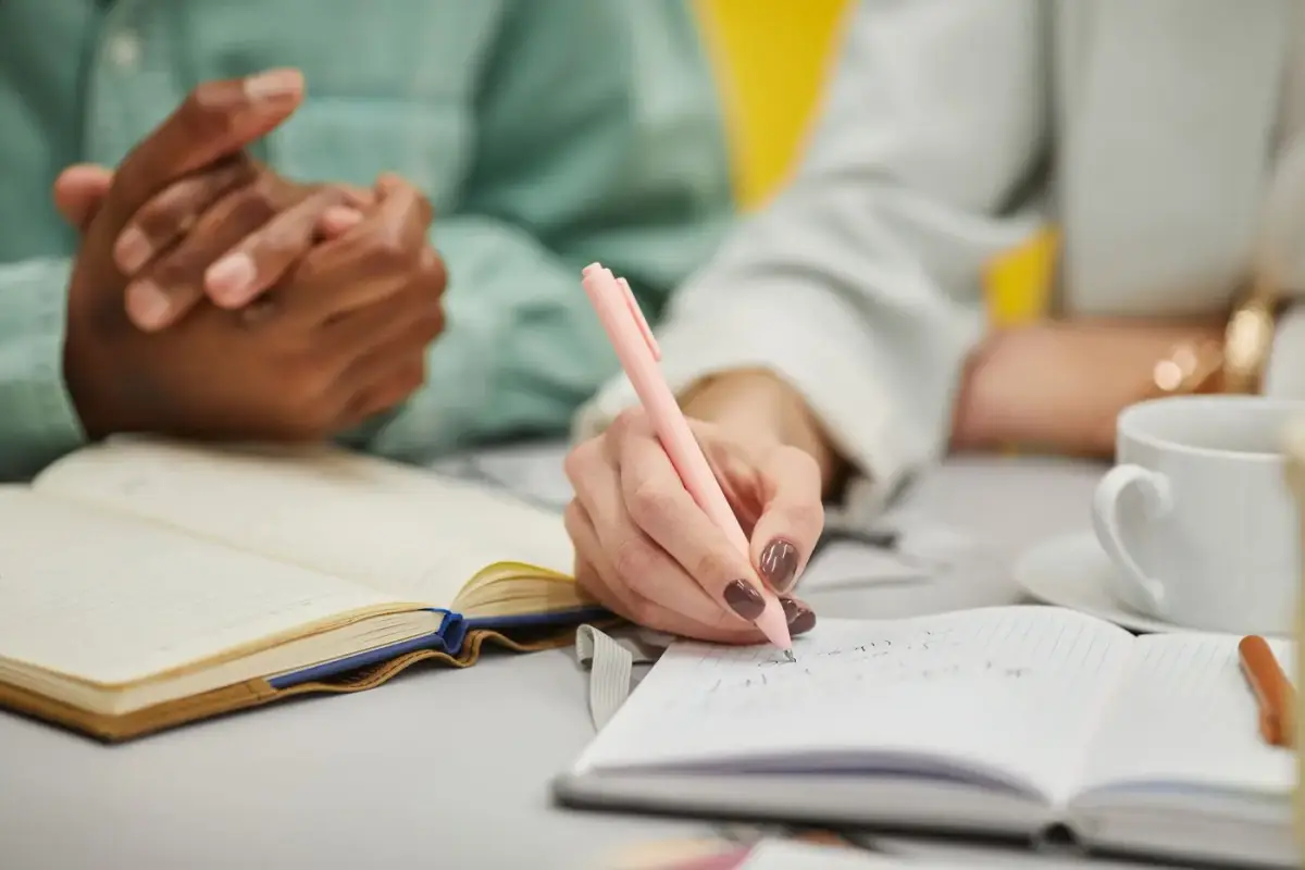 Hands writing plans and numbers in a notebook on a desk