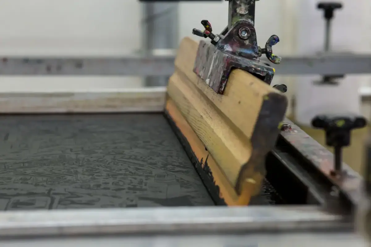 A screen printing setup with a wooden squeegee and screen