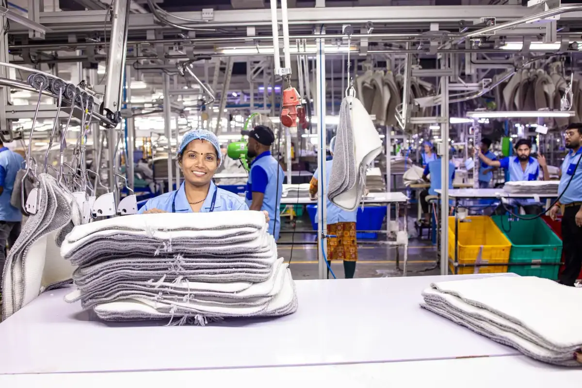 A worker in a textile production facility with stacks of folded garments