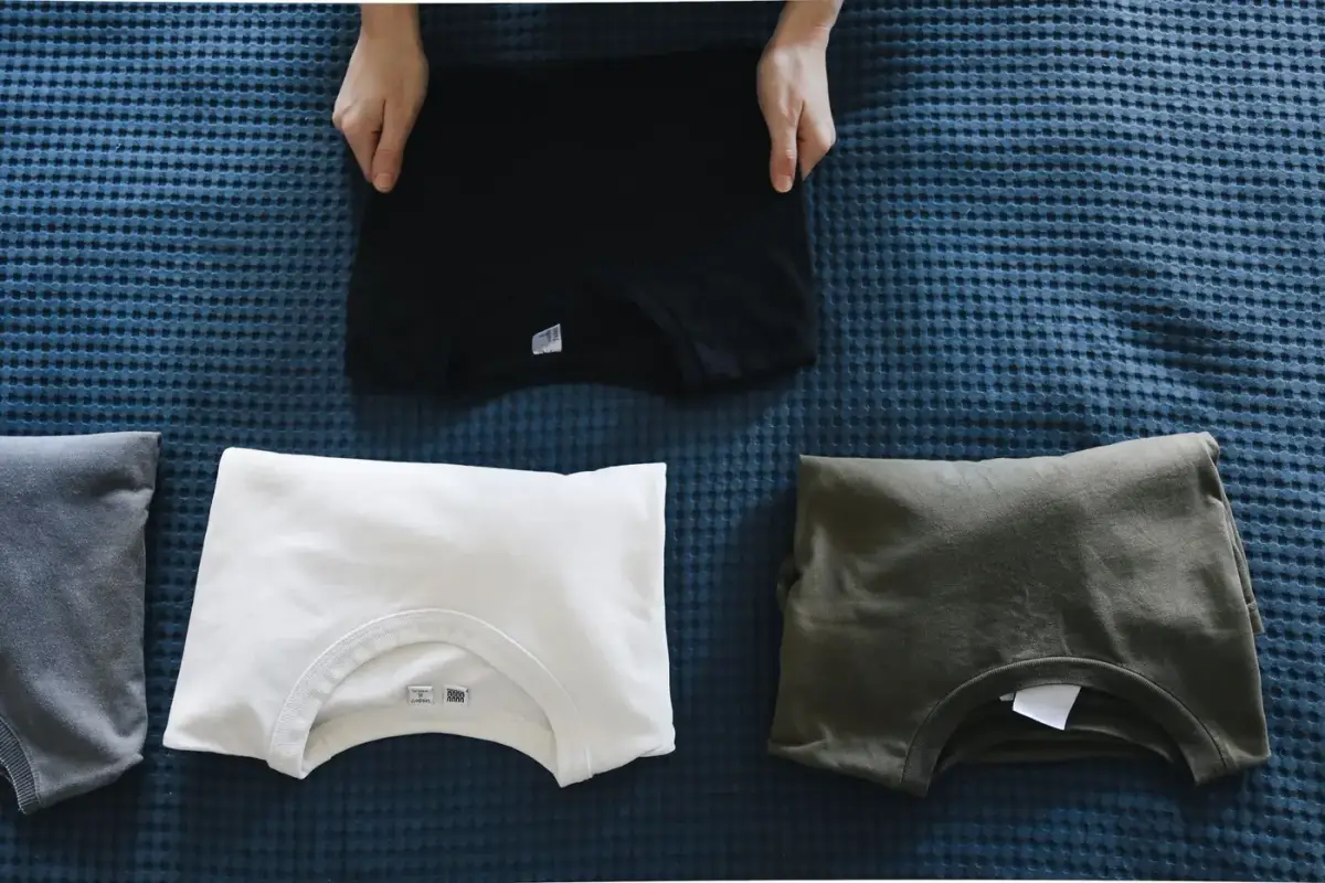 Neatly folded plain t-shirts in several colors laid out on a bed
