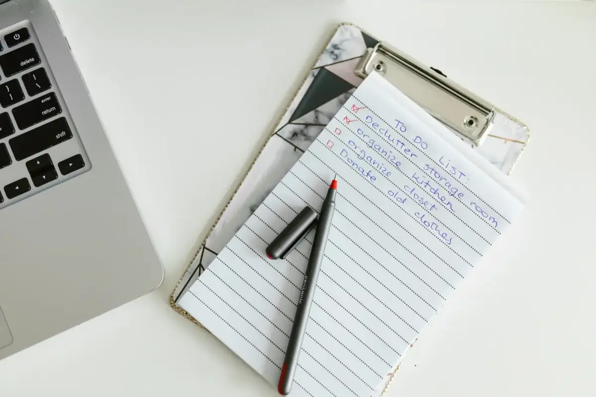 A to-do list on a clipboard beside a laptop and pen