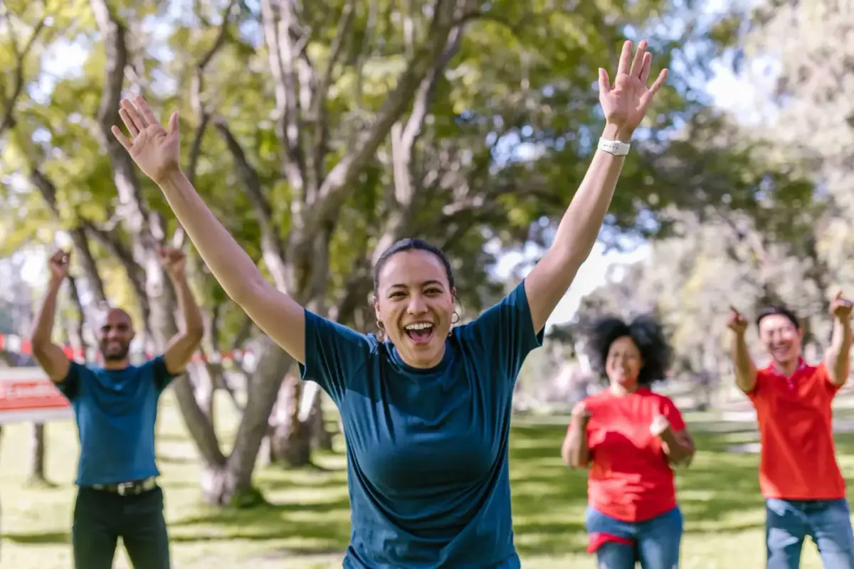 A group of people in matching colored shirts celebrating outdoors with raised arms
