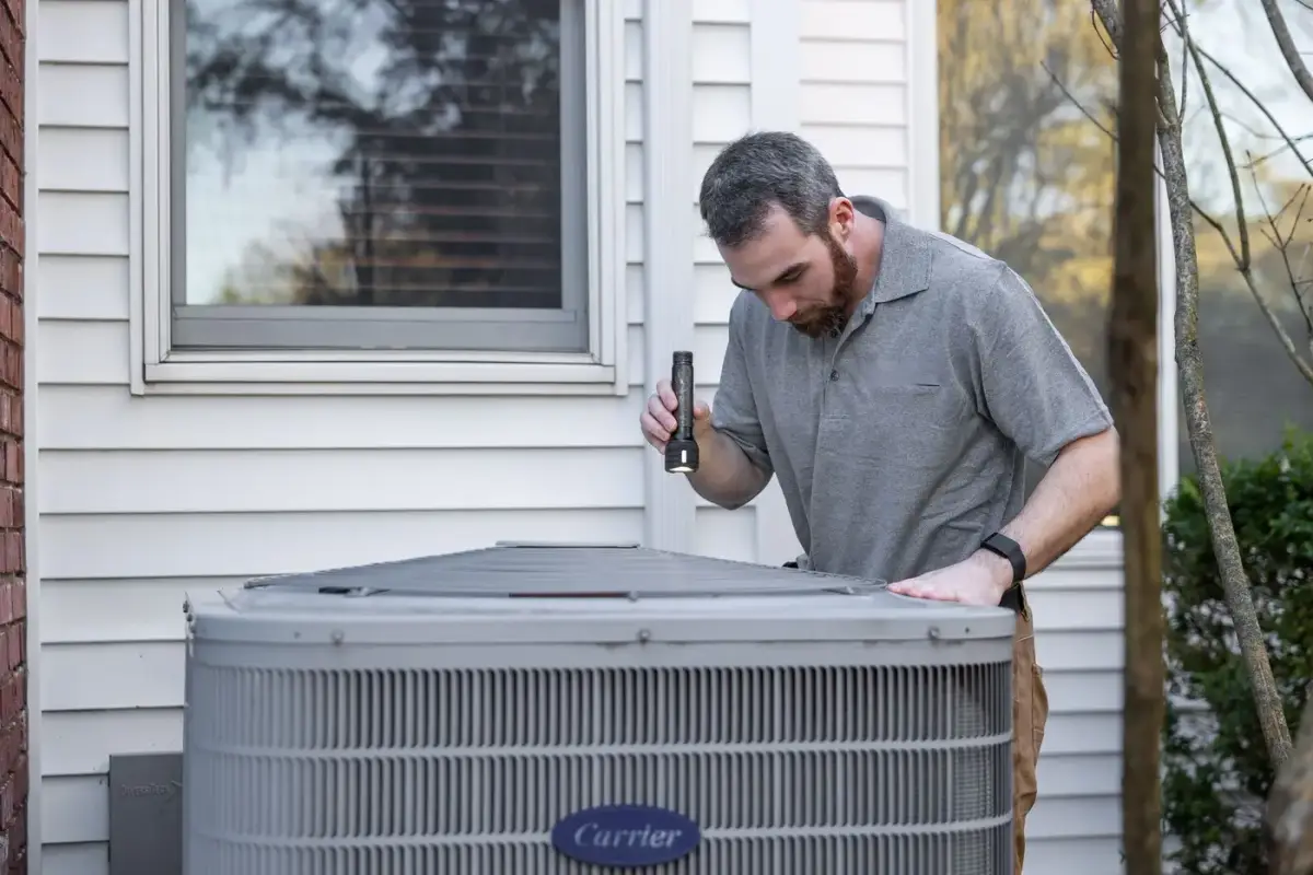 An HVAC technician inspecting an outdoor condenser unit at a home