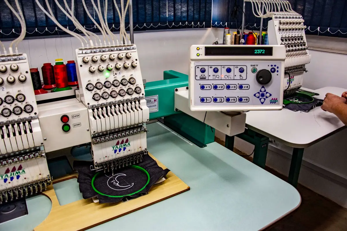 Industrial multi-head embroidery machines stitching a logo onto dark fabric in a workshop