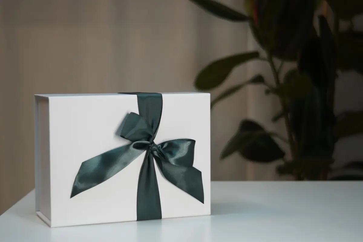 A white gift box tied with a wide dark green satin ribbon on a white table