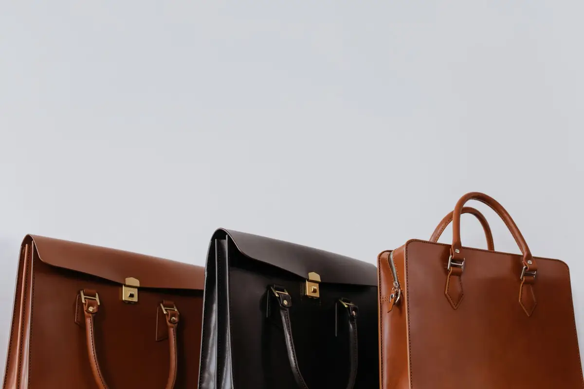 Three leather briefcases in tan, black, and cognac lined up against a gray wall