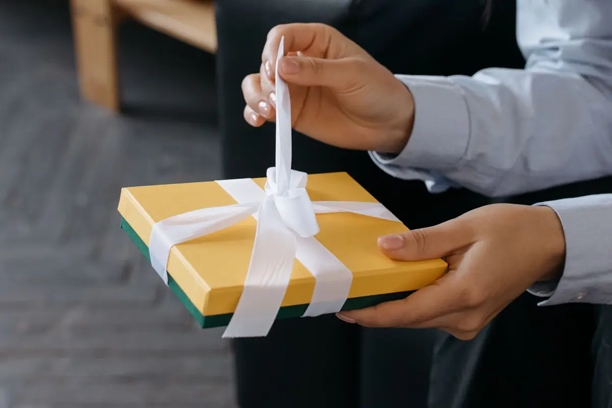 Hands untying a white ribbon on a yellow gift box