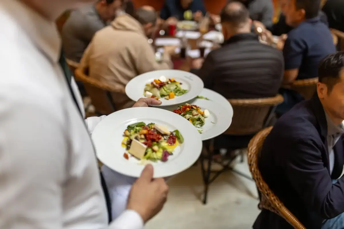 A waiter carrying plates of salad to guests at a restaurant table