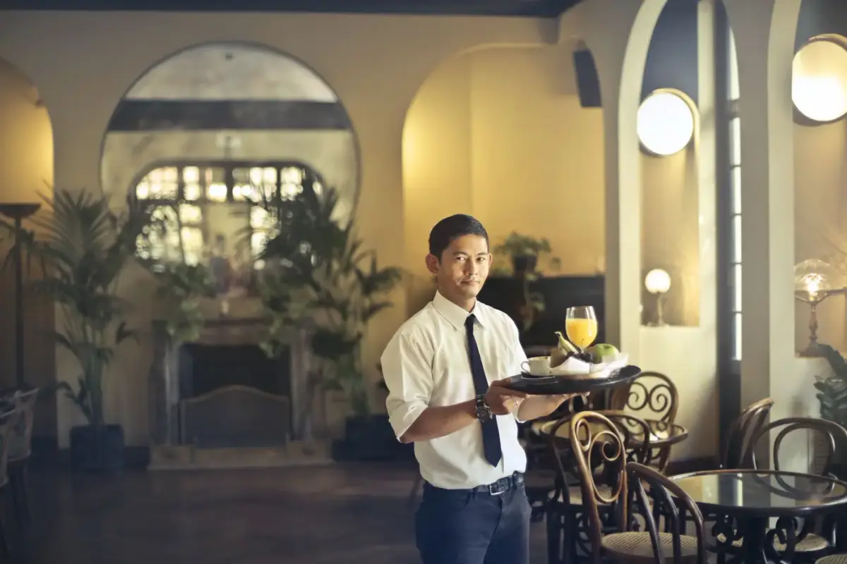 A restaurant waiter in a white shirt and tie carrying a tray in an elegant dining room