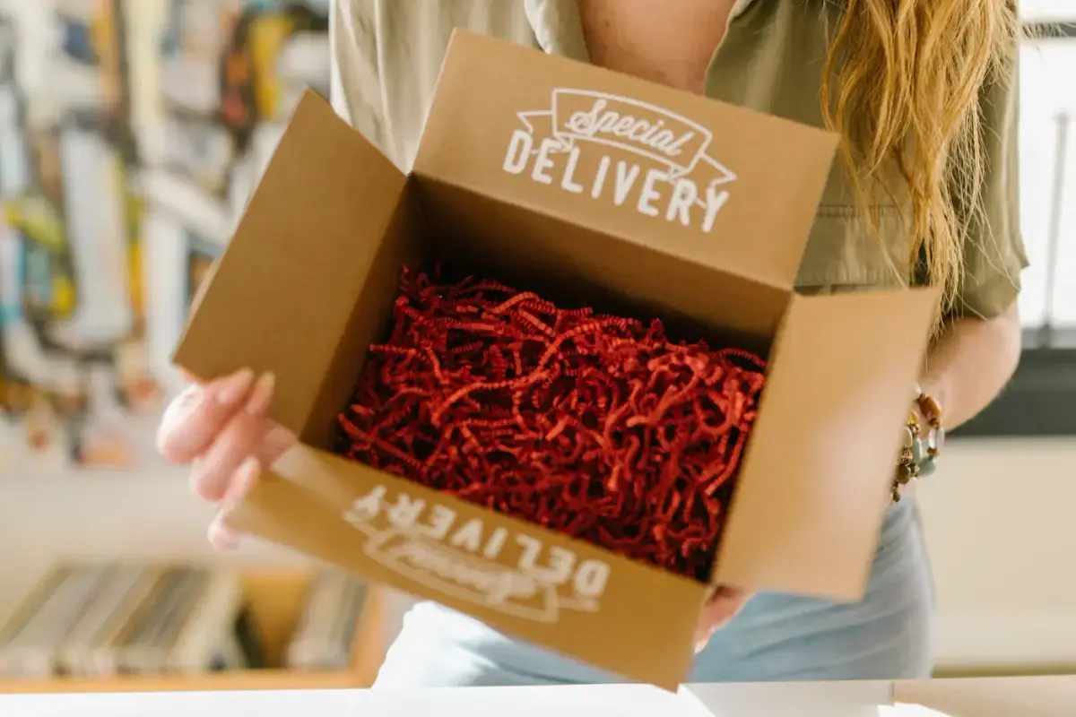 A person opening a branded delivery box filled with red crinkle paper