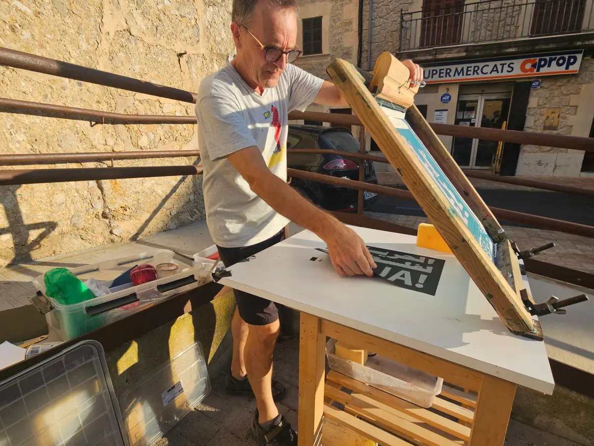 A man pulling a squeegee across a screen printing frame at an outdoor workbench