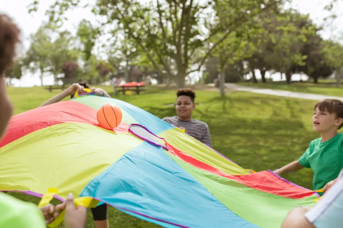 Campers holding the edges of a colorful parachute during an outdoor game