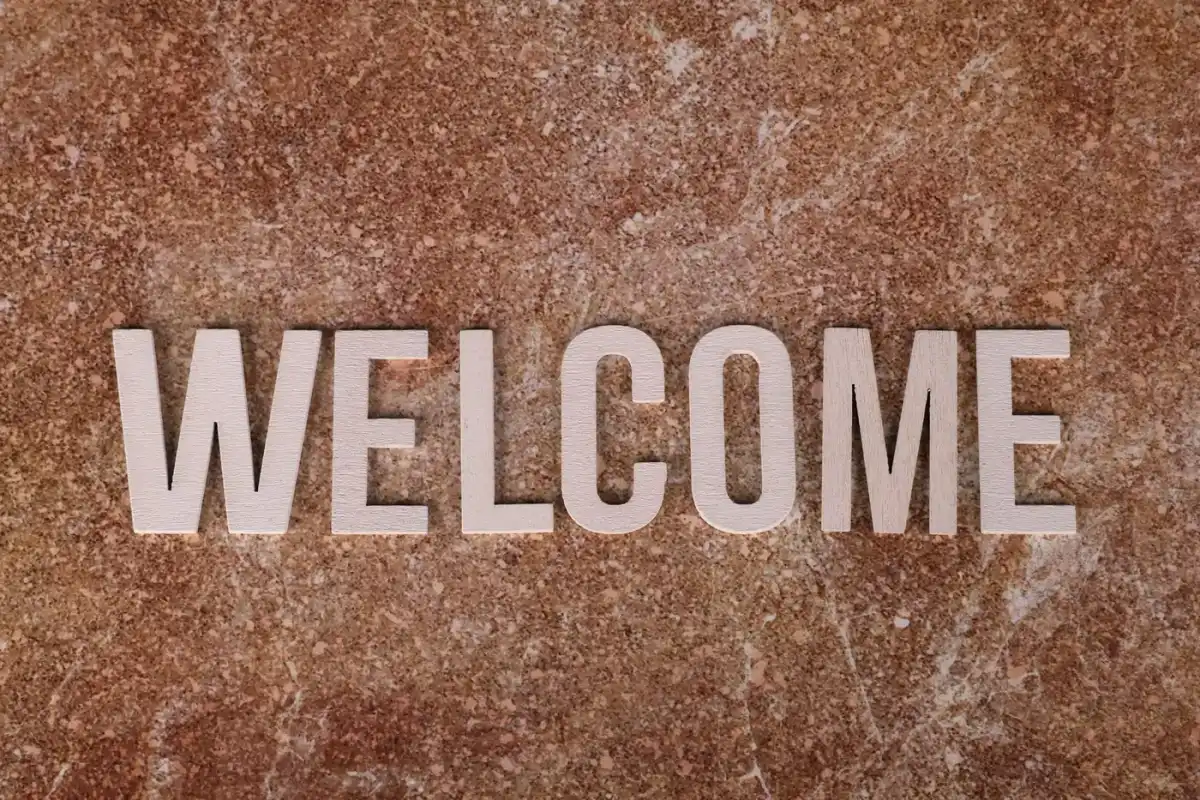 A wooden welcome sign against a textured stone background