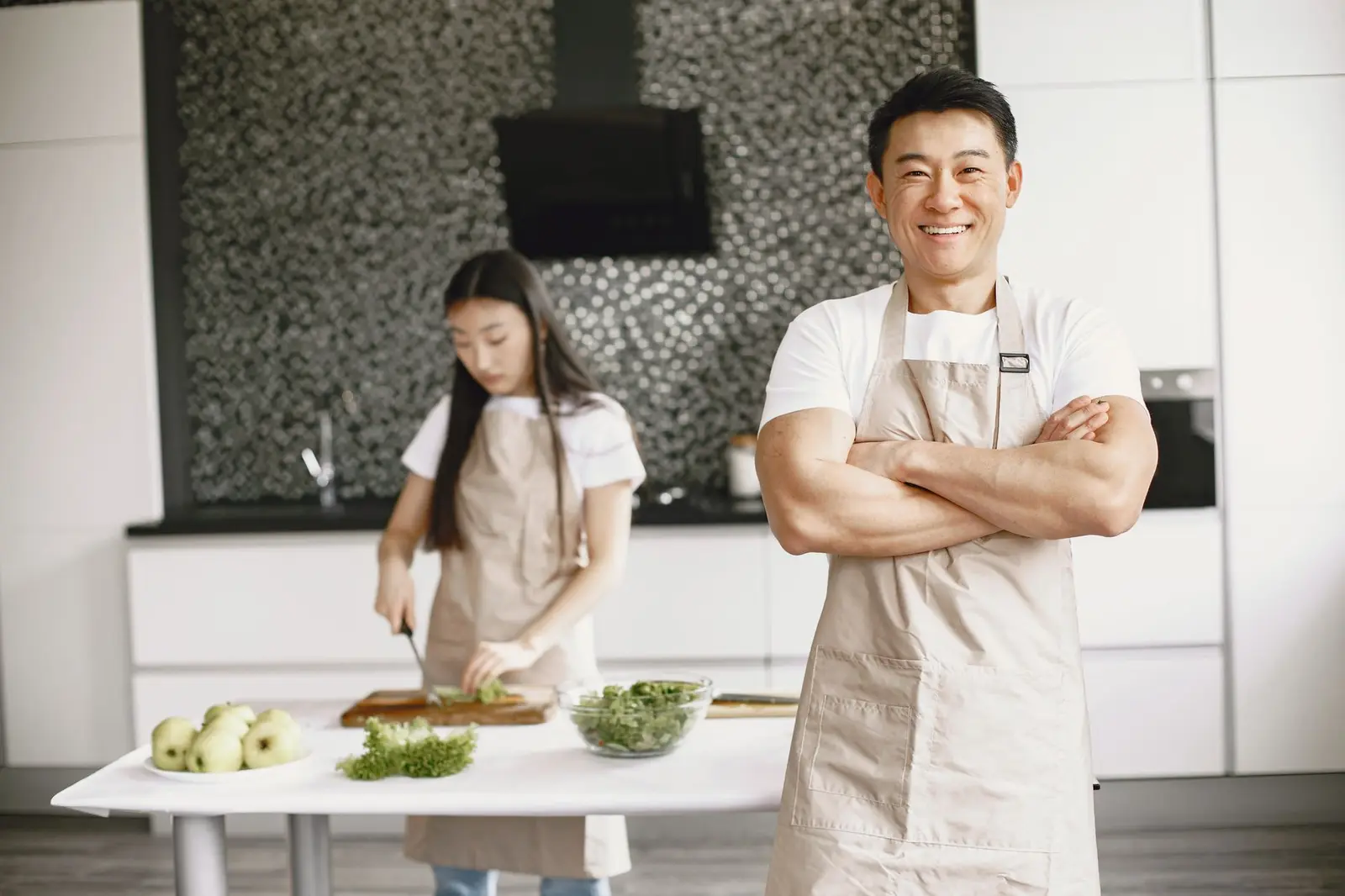 A smiling chef in a black bib apron in a modern restaurant kitchen