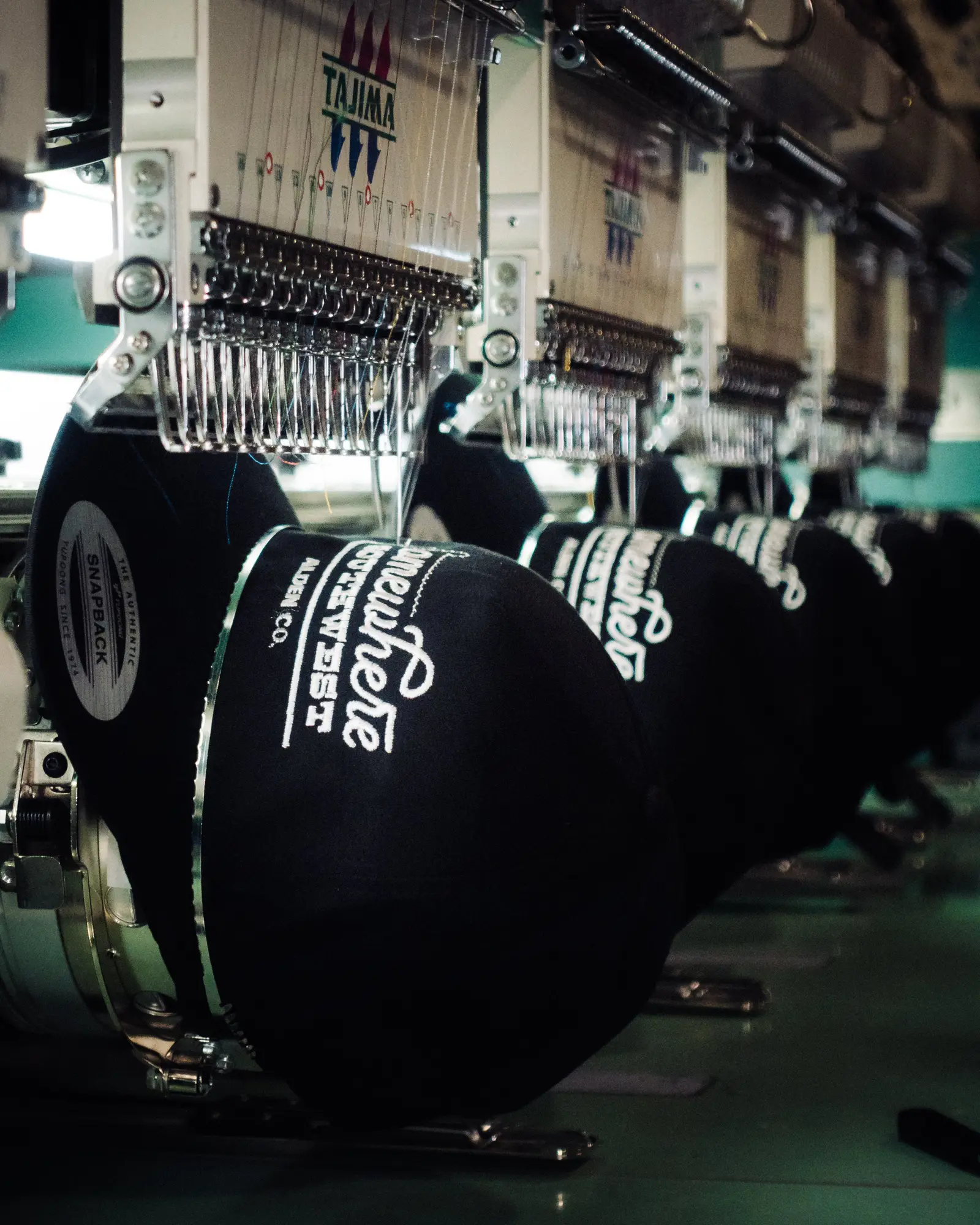 Branded caps being embroidered on a commercial machine in the Heart & Hook shop