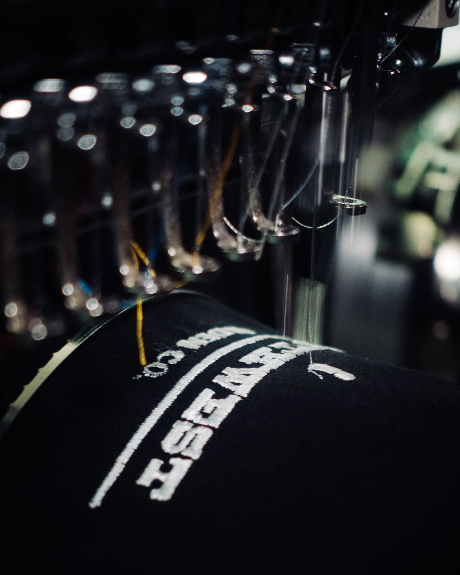 A cap logo being stitched on a commercial embroidery machine in the Heart & Hook shop